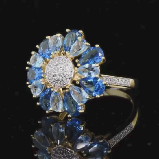 Gold ring shaped like a flower with alternating blue and clear pear-shaped stones around a pavé-set centre


