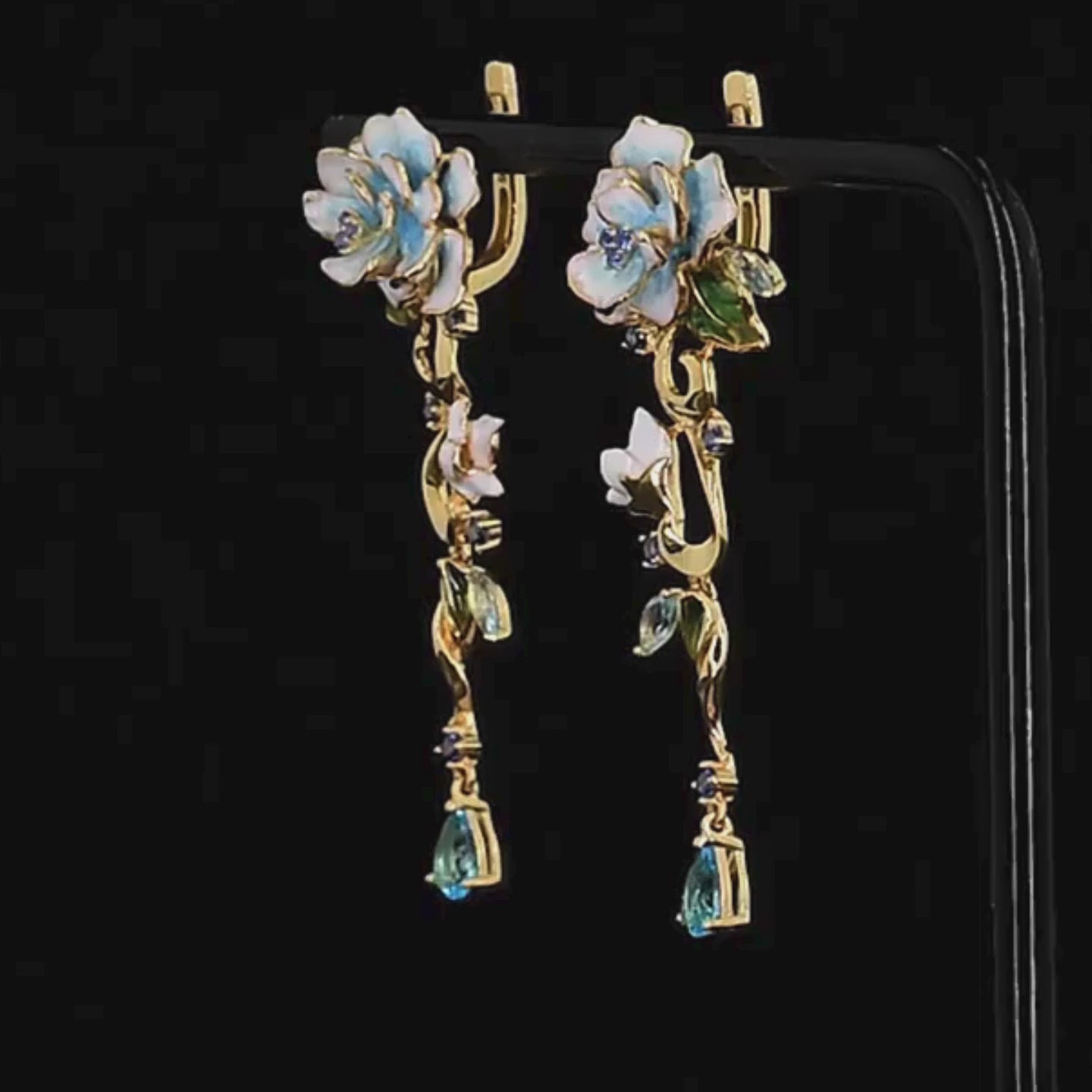 Gold floral earrings with hand-painted white and blue enamel petals, sapphire accents, and dangling blue teardrop stones

