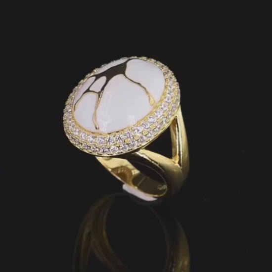 Gold ring with a large white stone featuring golden vein-like patterns, encircled by two rows of clear stones.

