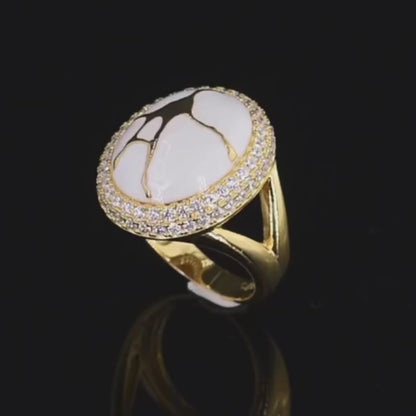 Gold ring with a large white stone featuring golden vein-like patterns, encircled by two rows of clear stones.

