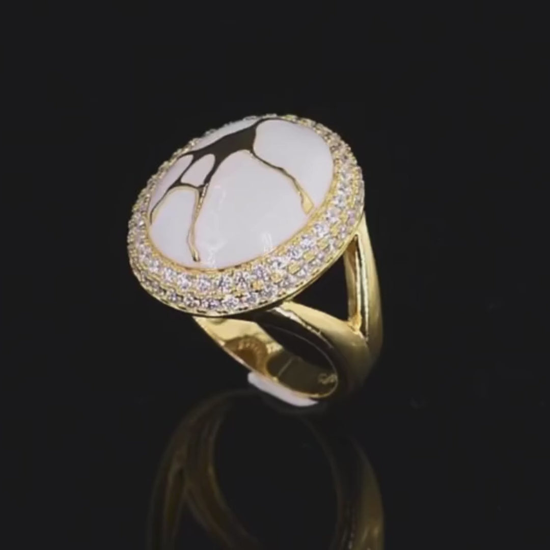 Gold ring with a large white stone featuring golden vein-like patterns, encircled by two rows of clear stones.


