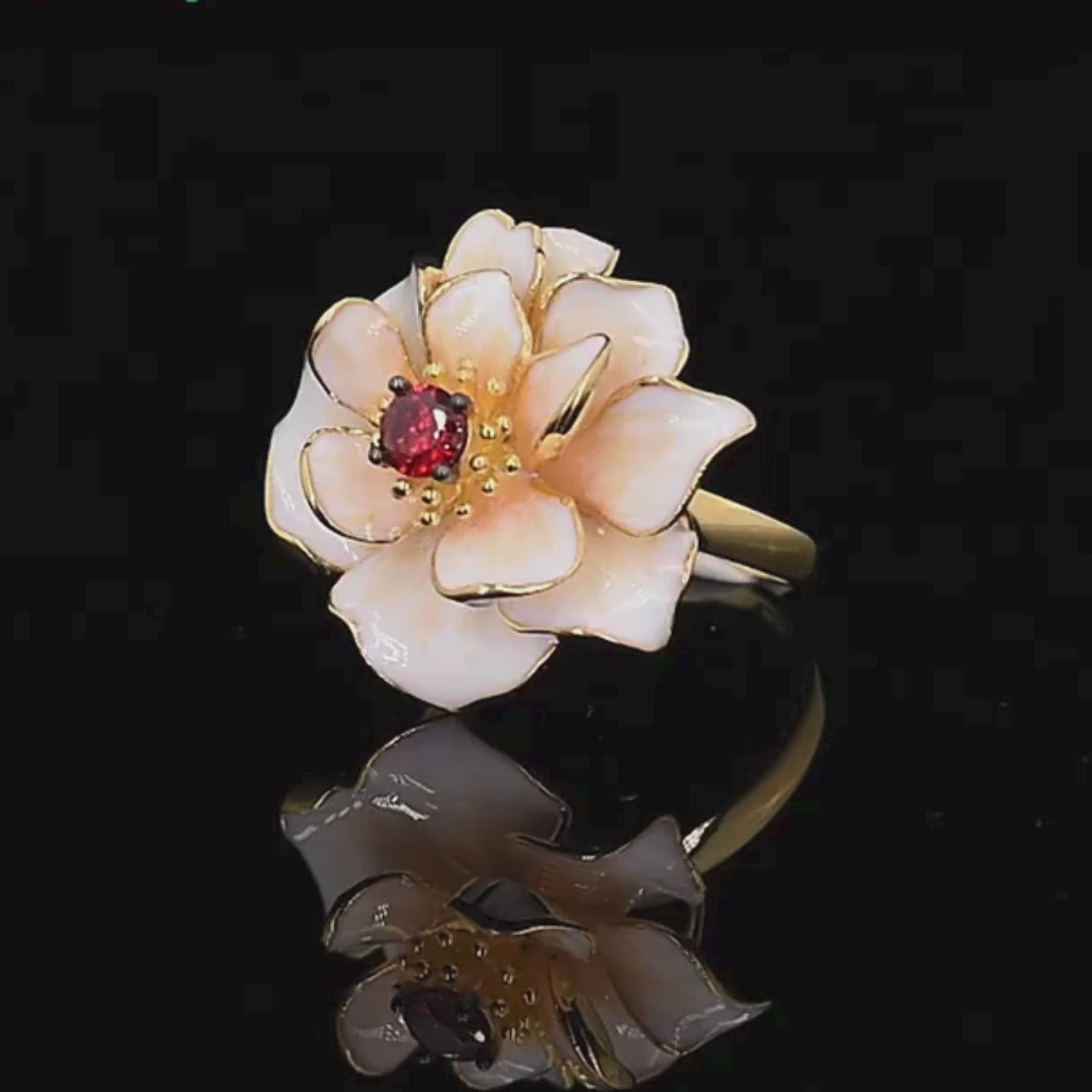 Gold ring with layered white enamel flower petals and a red gemstone at the center.

