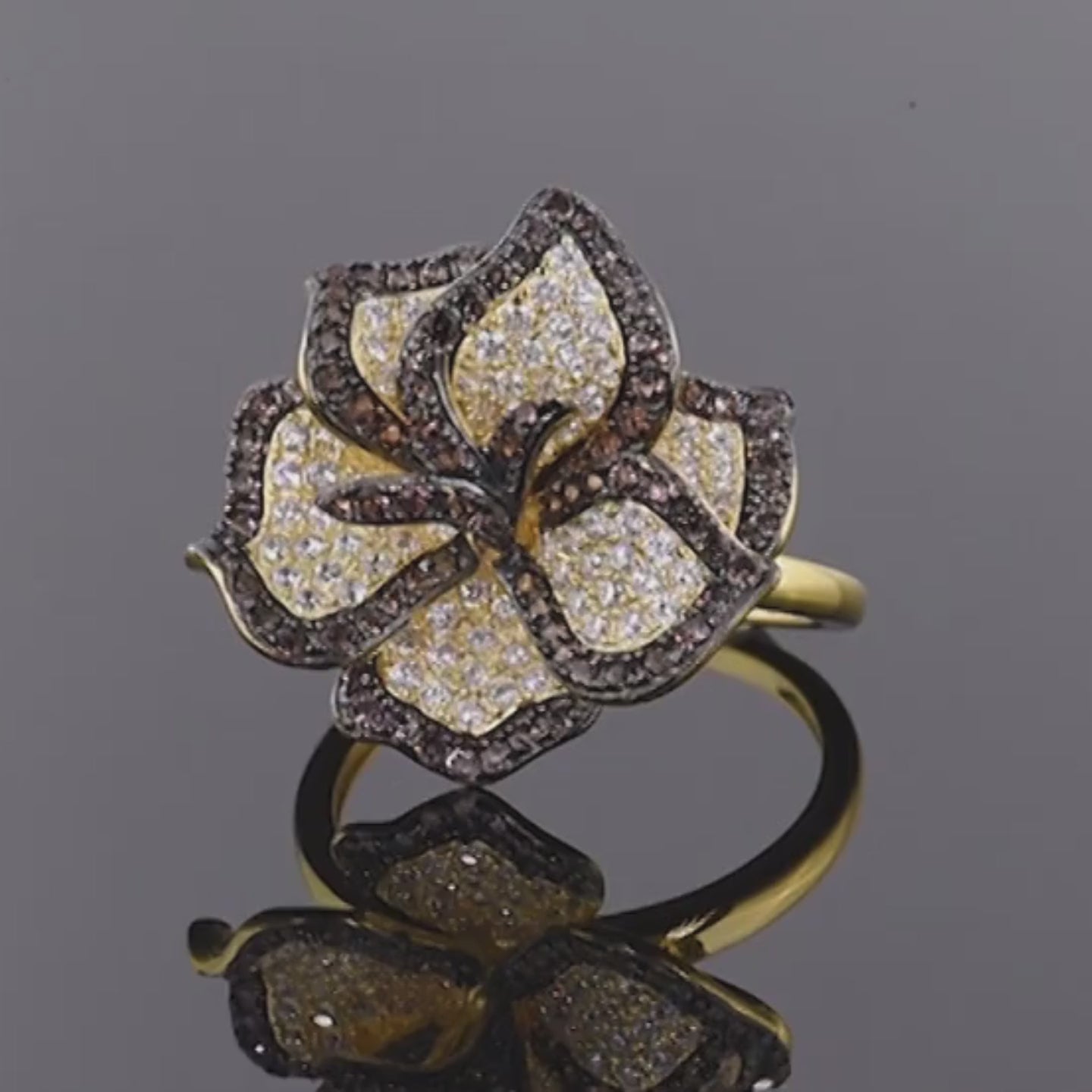 Gold ring with a large, sparkling flower design featuring white and brown stones on each petal.

