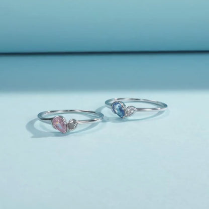 Sterling silver ring with a pear-shaped blue stone and round white stone set side by side
Sterling silver ring featuring a pink teardrop stone paired with a round clear stone in an open-heart inspired setting.


