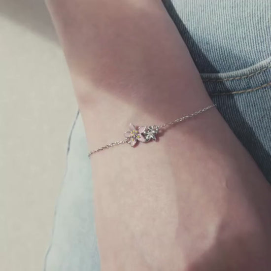 Delicate silver bracelet featuring two small pink cherry blossom charms on a fine chain.

