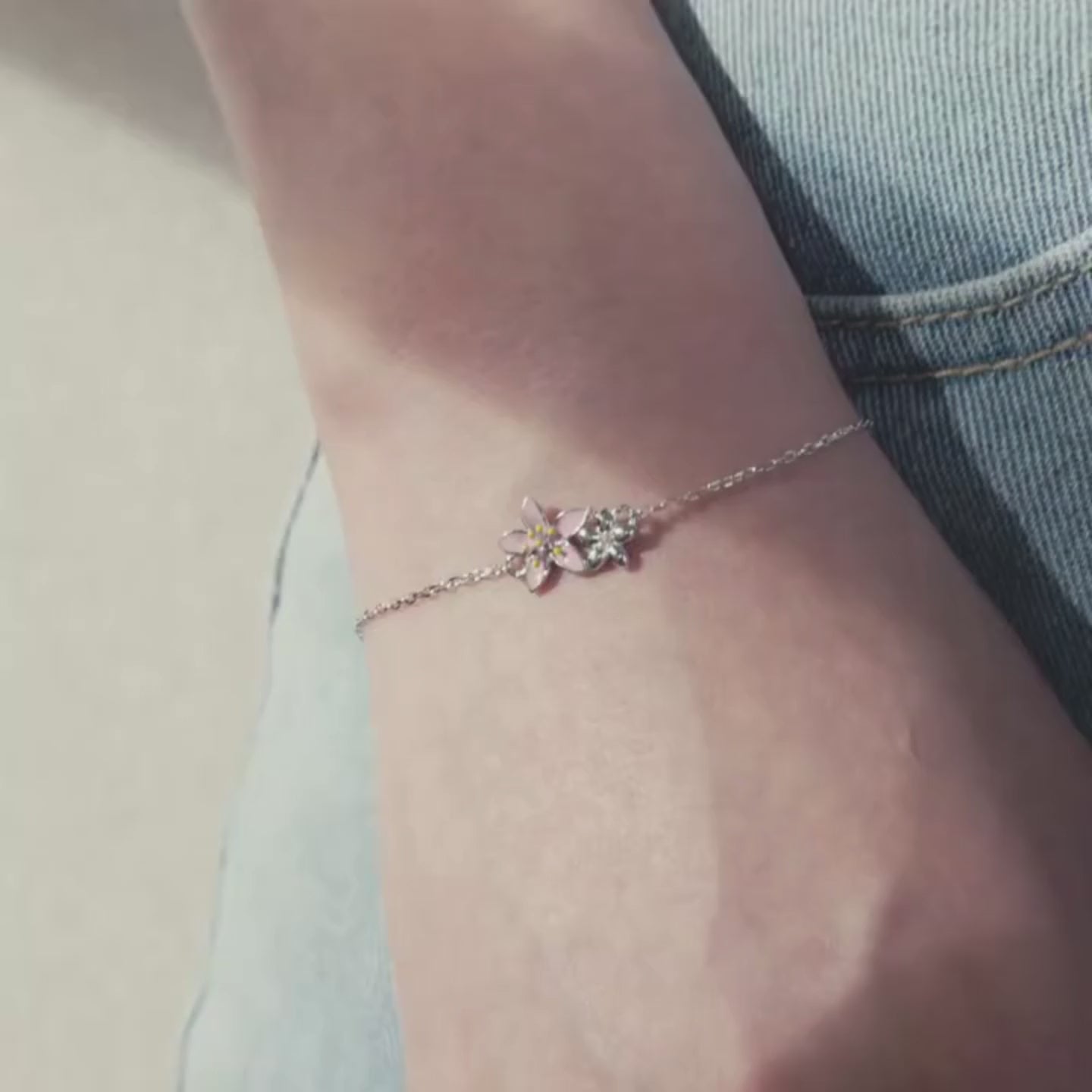 Delicate silver bracelet featuring two small pink cherry blossom charms on a fine chain.

