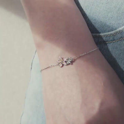 Delicate silver bracelet featuring two small pink cherry blossom charms on a fine chain.

