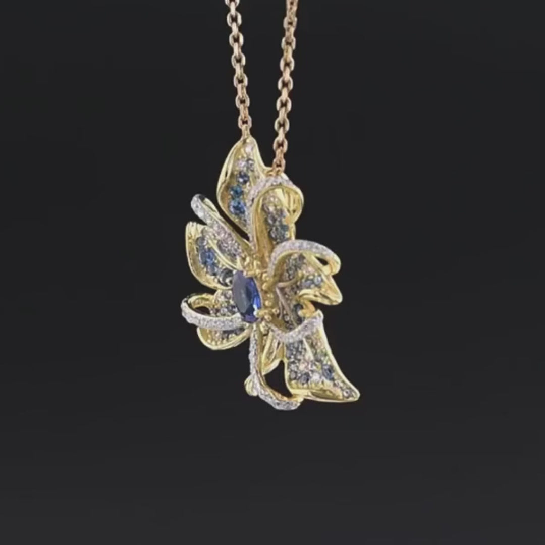 Gold floral brooch with layered petal-like curves, set with blue gemstones and clear pavé accents, featuring an oval sapphire-blue centerpiece