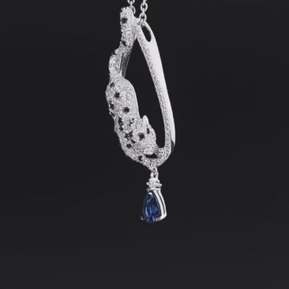 Leopard-shaped silver pendant with black stone spots, set within a teardrop frame and finished with a hanging blue teardrop gemstone.

