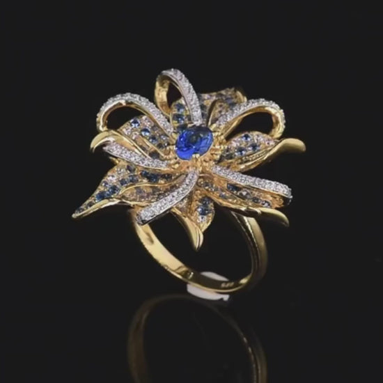 Gold ring in the shape of a flower with pavé blue and white stones and a central oval gem


