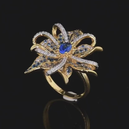 Gold ring in the shape of a flower with pavé blue and white stones and a central oval gem

