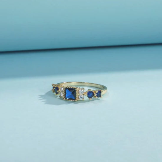 Gold-plated sterling silver ring with a central square-cut deep blue stone and surrounding clear round stones

