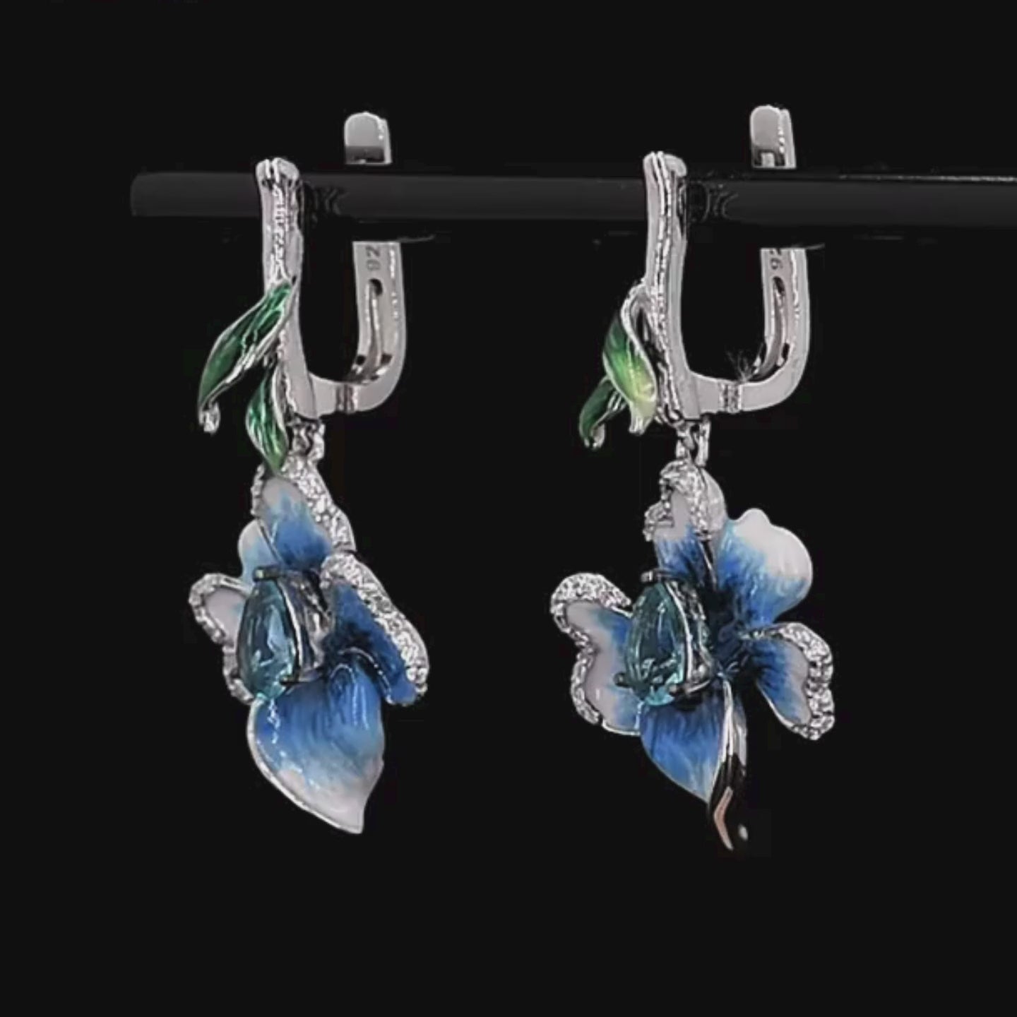 Silver floral earrings with hand-painted blue petals, green enamel accents, and teardrop blue stones.

