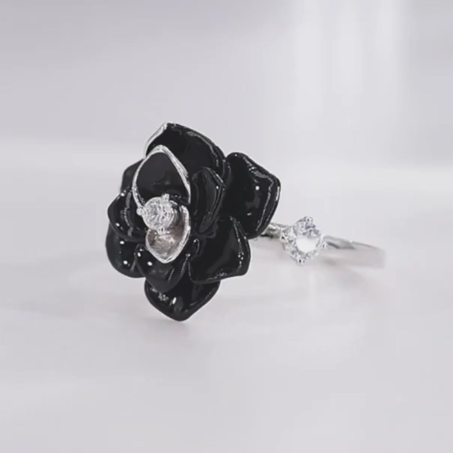 Silver ring with a black enamel rose centerpiece and two clear gemstones on the band.

