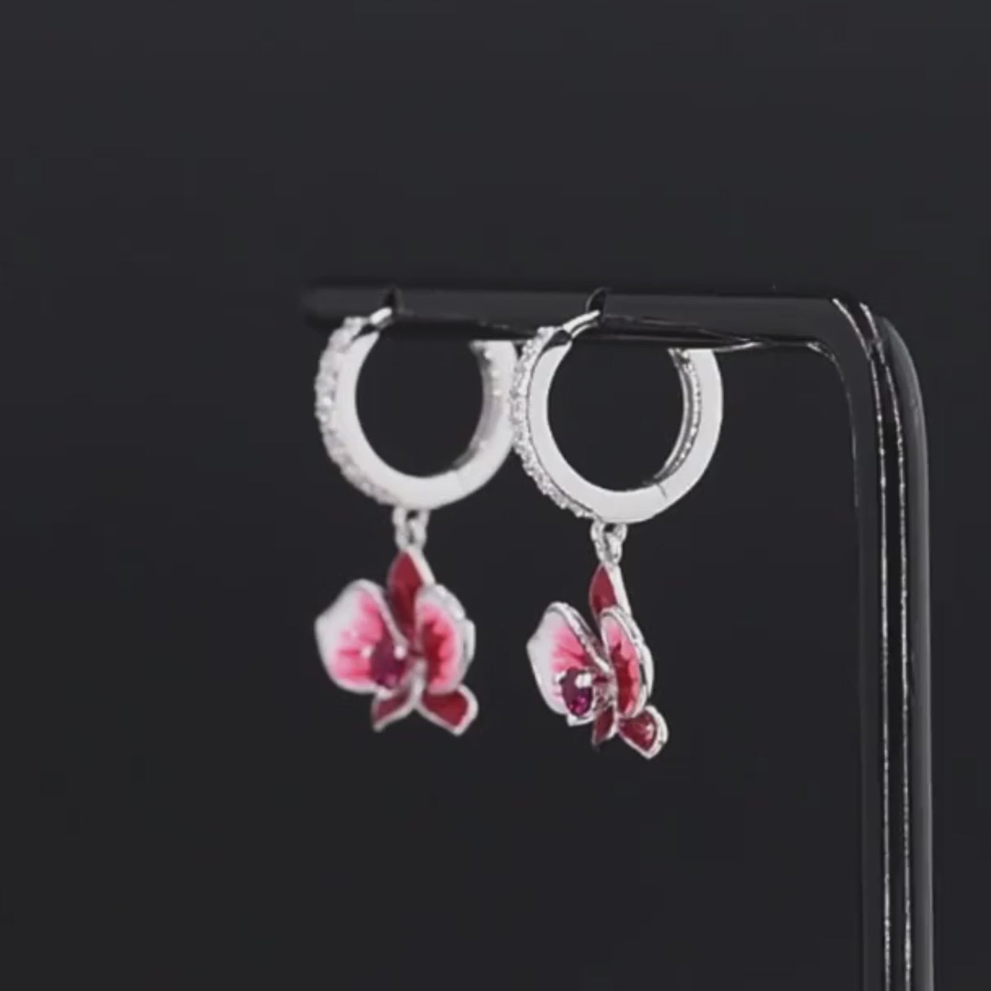 Cuore Rubino earrings featuring red and pink orchid-shaped enamel flowers with sparkling red gemstone centers and crystal-accented hoops.

