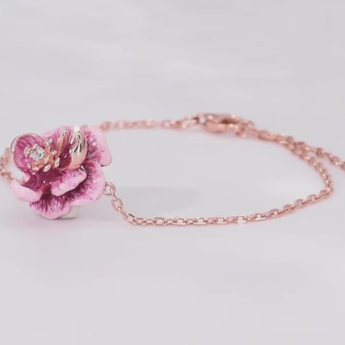 Anemone bracelet with a delicate chain and a central pink flower charm detailed with enamel and a sparkling center stone.

