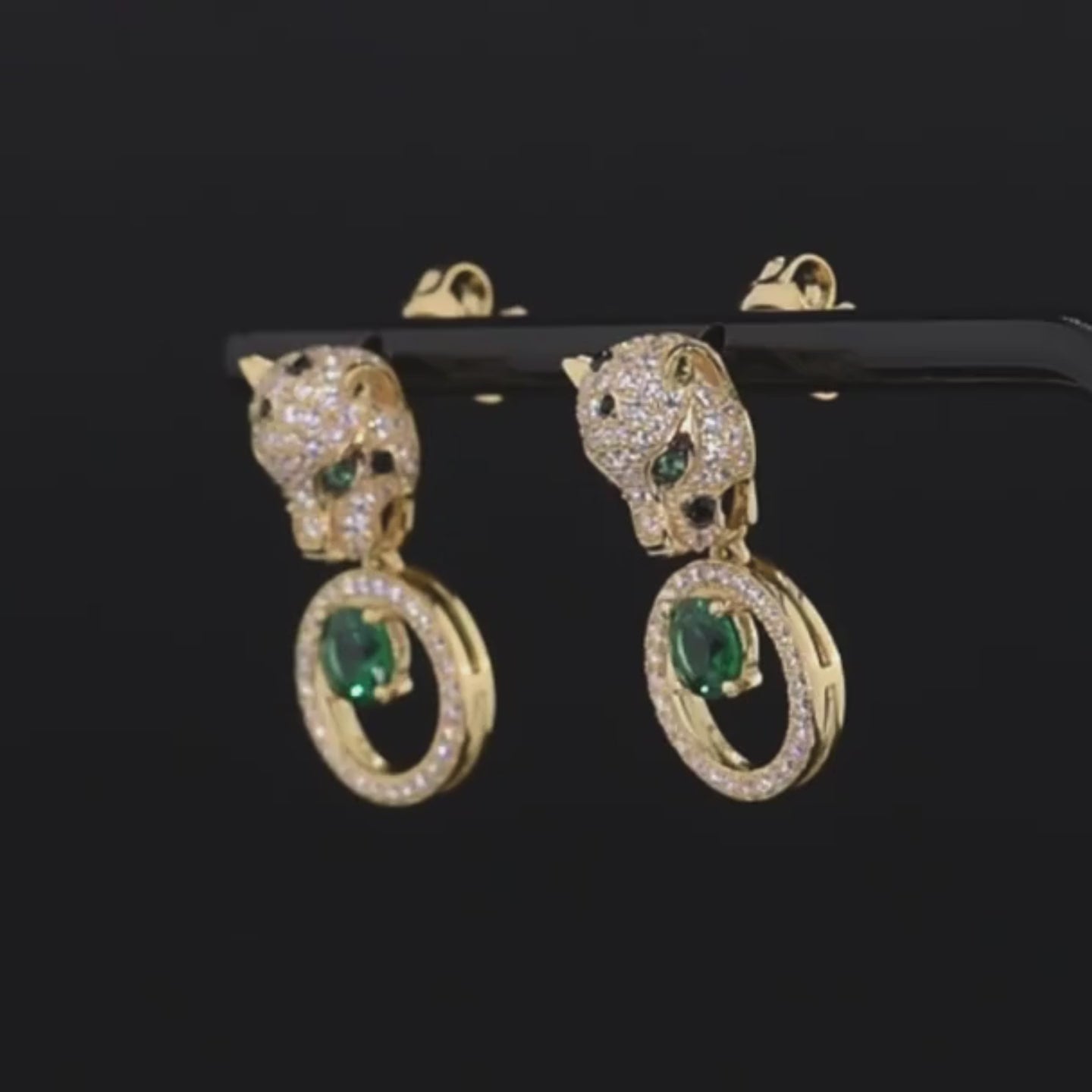 Gold earrings with panther head design, sparkling black and white stones, and green gemstone drop in circular setting

