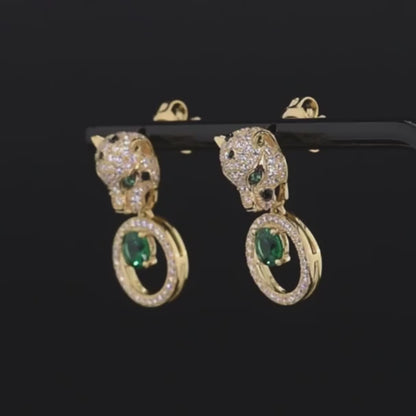 Gold earrings with panther head design, sparkling black and white stones, and green gemstone drop in circular setting

