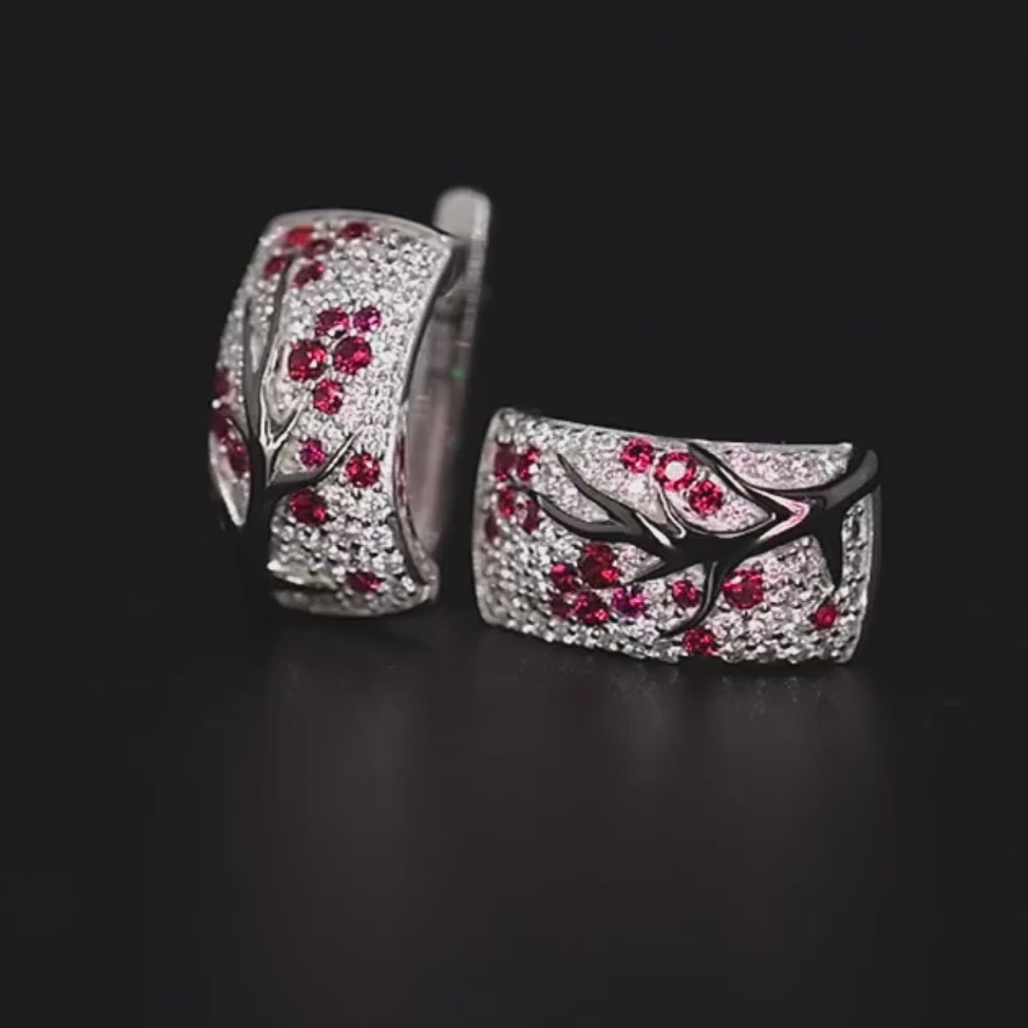 Silver earrings featuring raised black branches with scattered red blossom-like stones.

