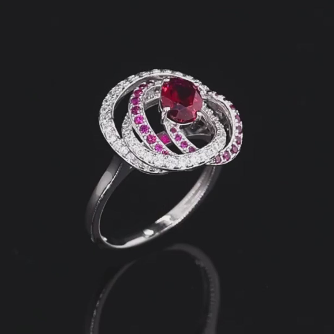 Vermiglio ring with a vivid red oval gemstone at the center, wrapped in spiraling bands of white and red stones set in silver.


