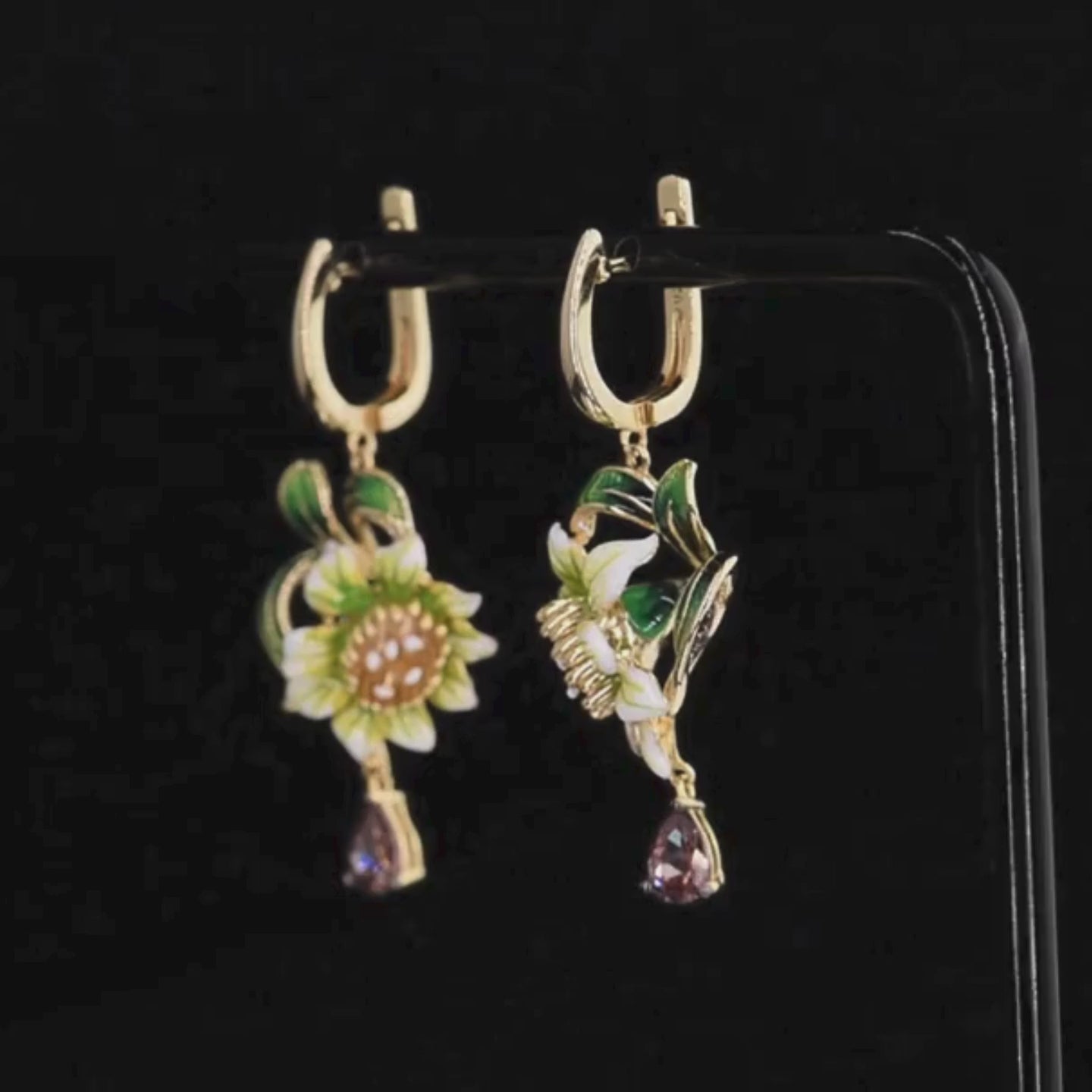 Gold drop earrings featuring white enamel flowers, green leaf detailing, and teardrop gemstones

