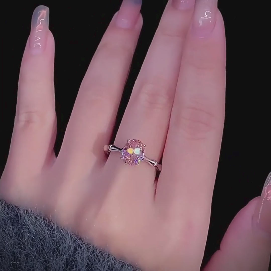 Silver band ring with an oval-cut pink-orange tourmaline stone, displayed against a deep red background from the Rossa collection.

