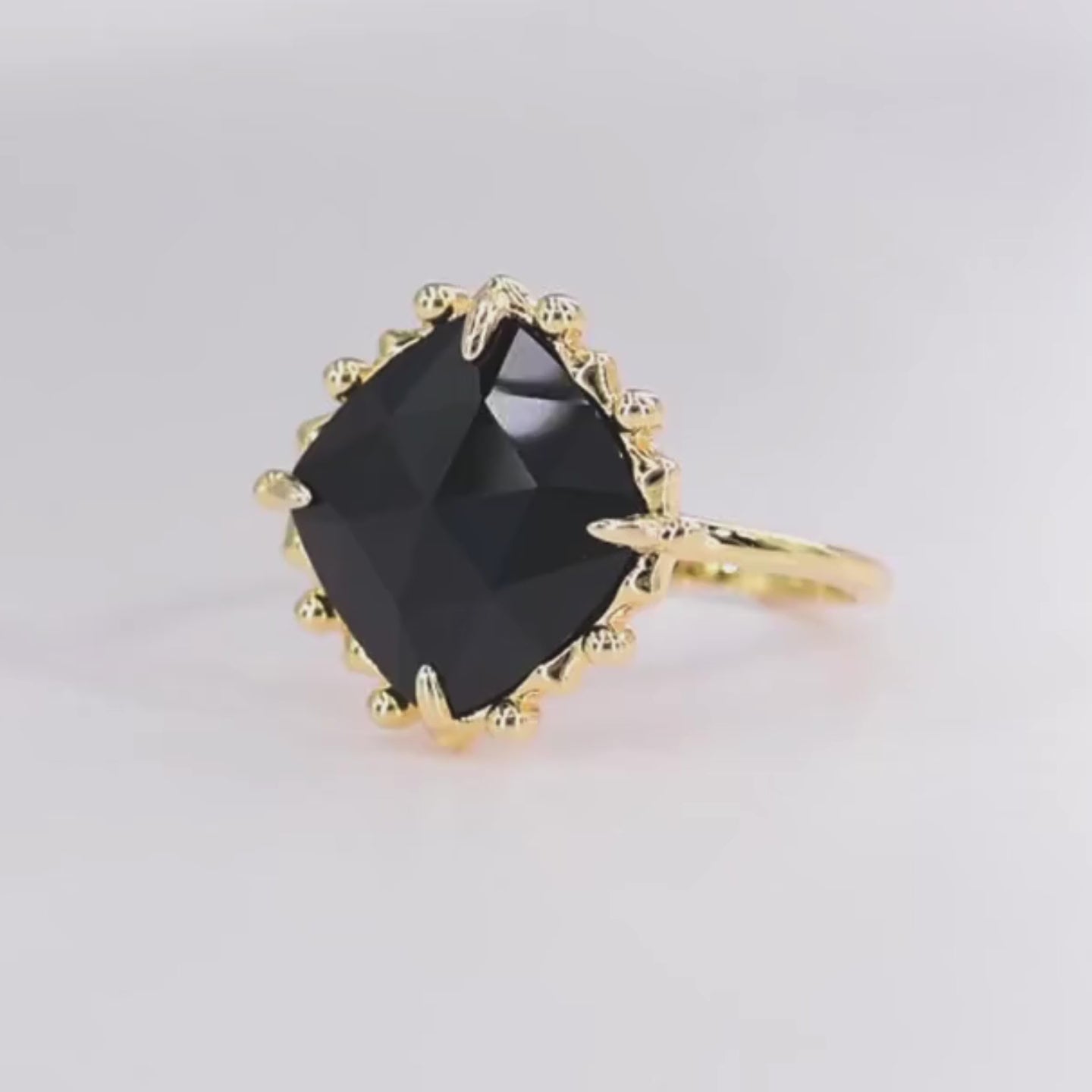 Gold ring with a large cushion-cut black stone and decorative claw prongs.


